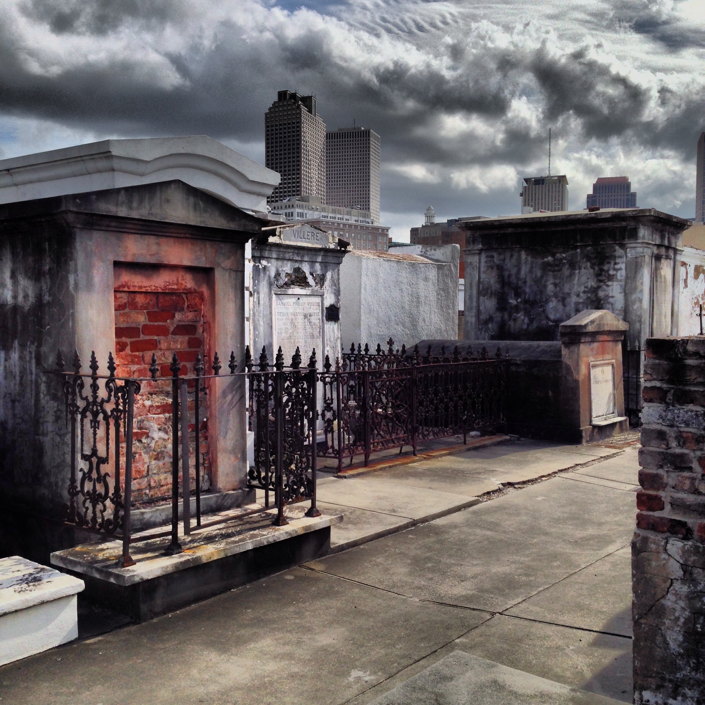 St. Louis Cemetery, New Orleans, tombs beneath a storm sky with the downtown skyline behind.