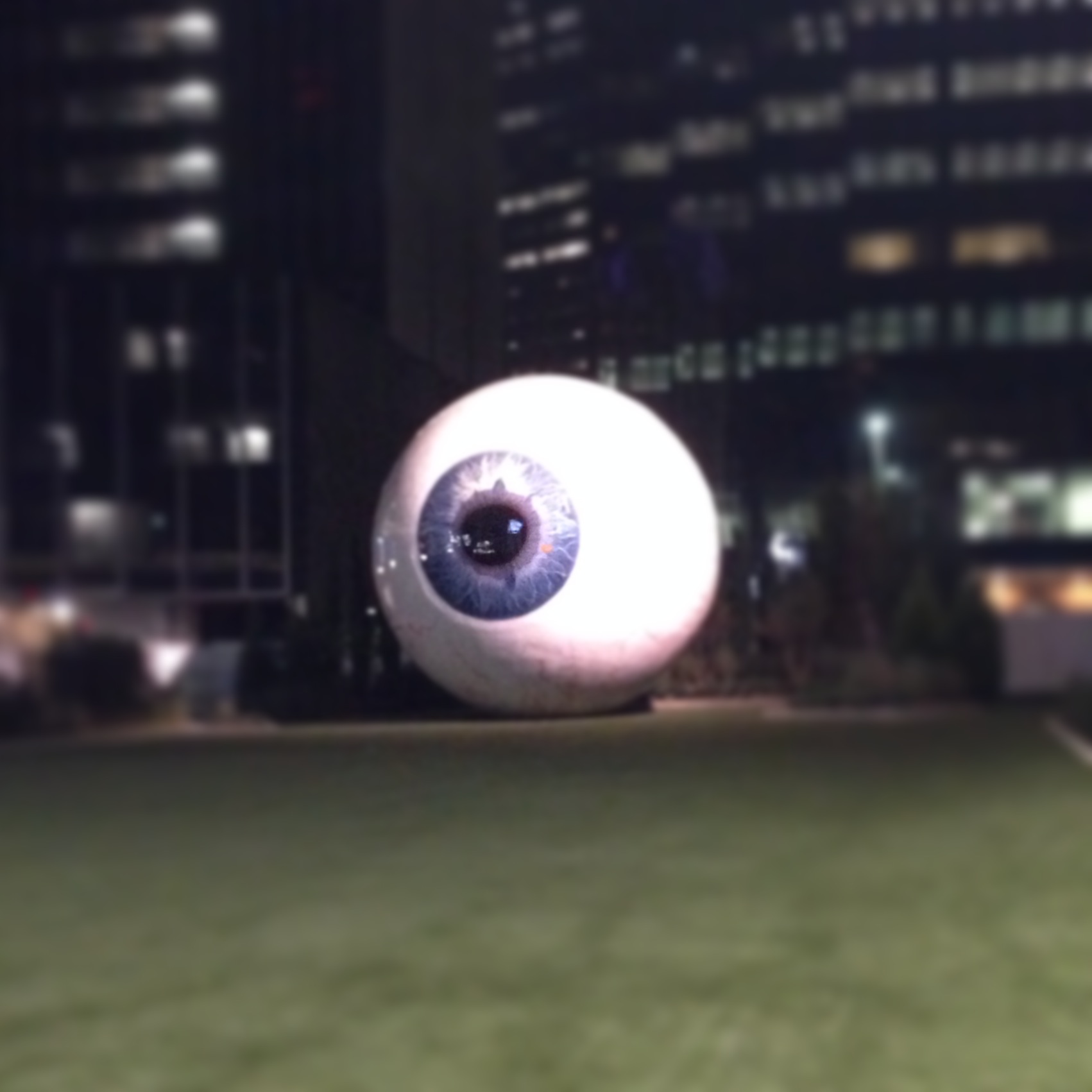 A large sculptural eyeball lit up at night against a city skyline.