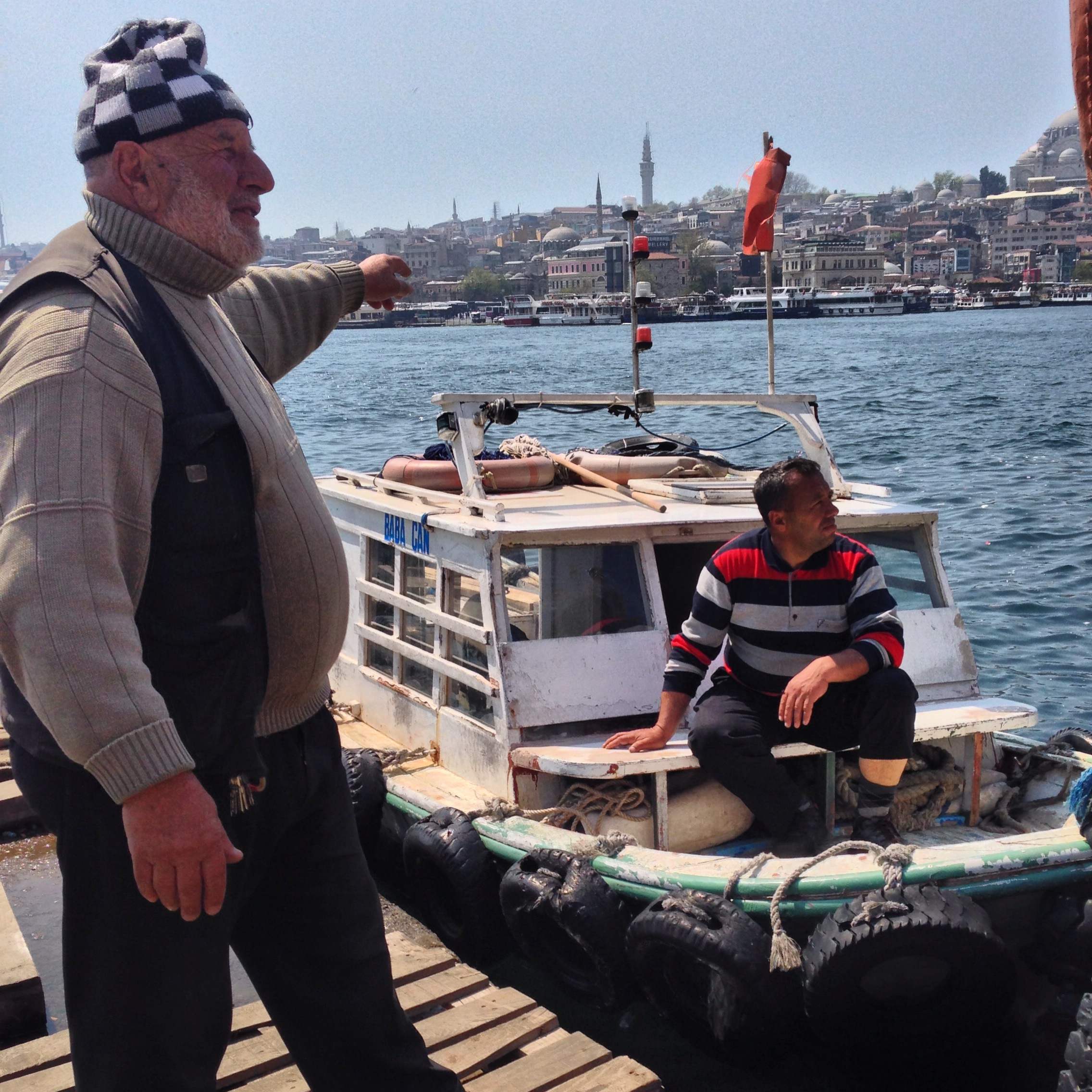 Two fishermen on a boat on the Bosphorus, Istanbul, with the city skyline behind them.