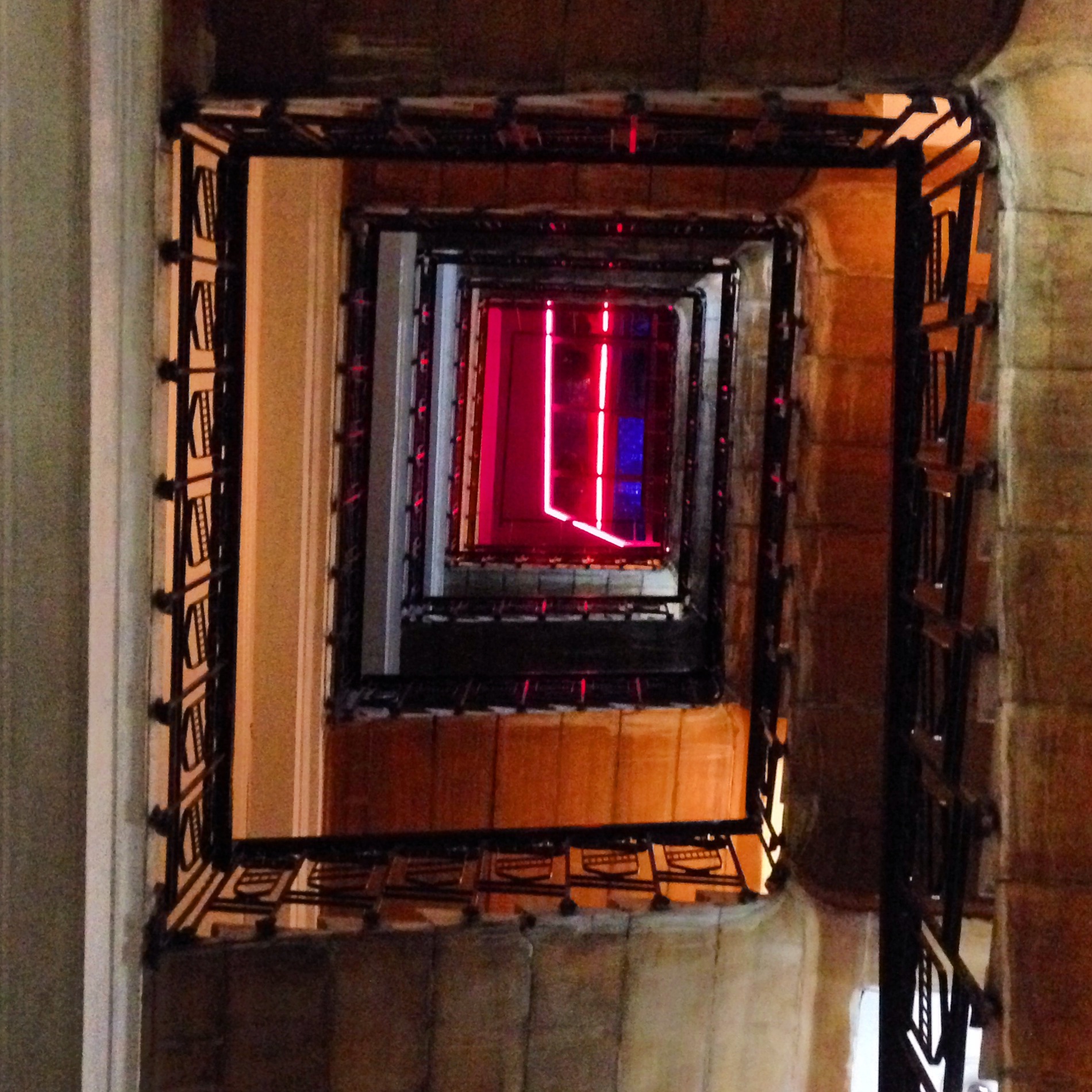 A square spiral stairwell viewed from above, red neon glowing at the center.