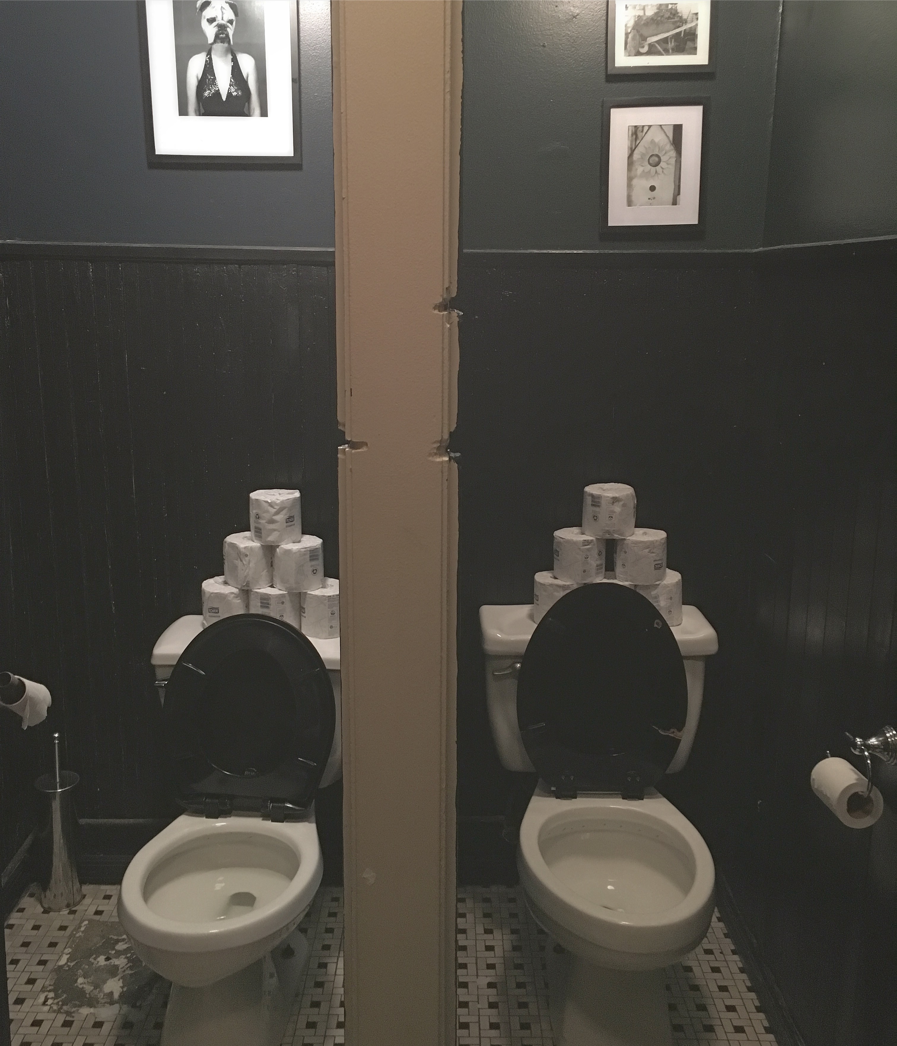 Two toilets in adjoining stalls, each stacked with rolls of toilet paper.